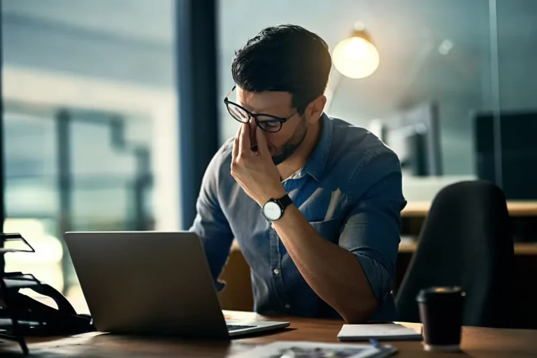 Stressed professional sitting at a laptop and holding his head in an office