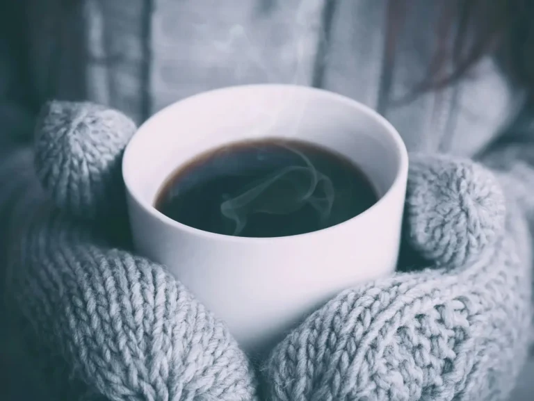 Hot drink held in a warm knitted blanket, representing the comfort of attending therapy from home