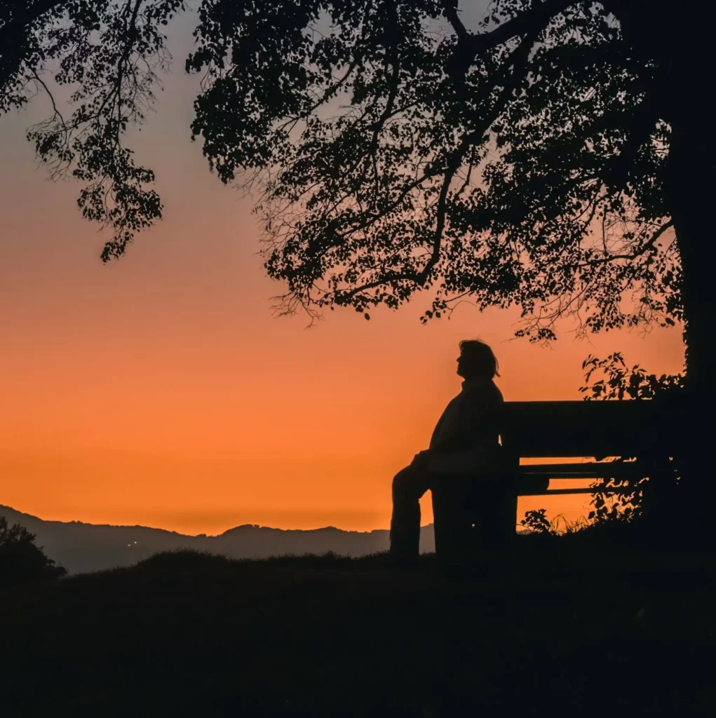 Person sitting alone on a bench and reflecting at sunset