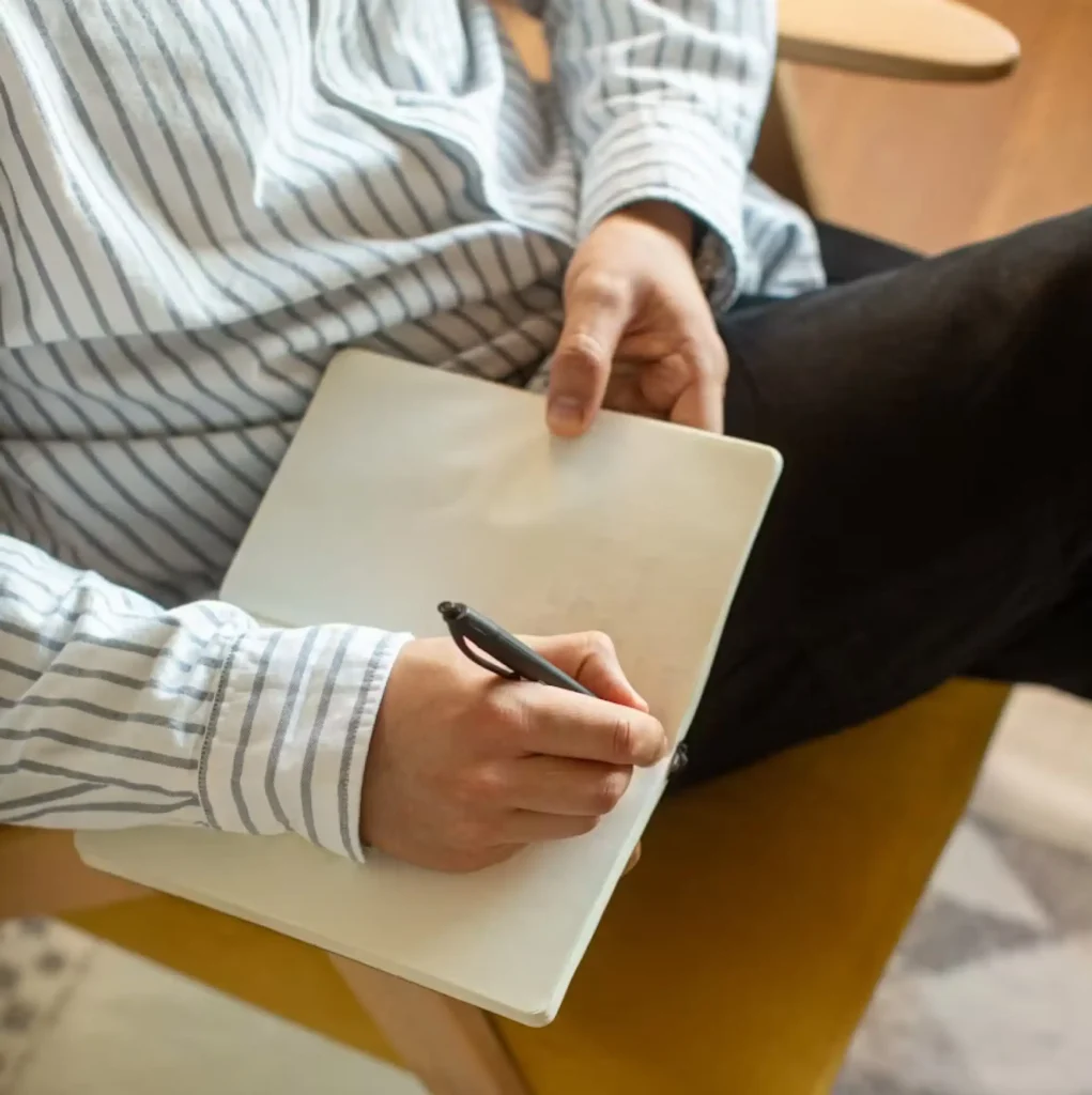 Person writing in a notebook during a reflective therapy exercise