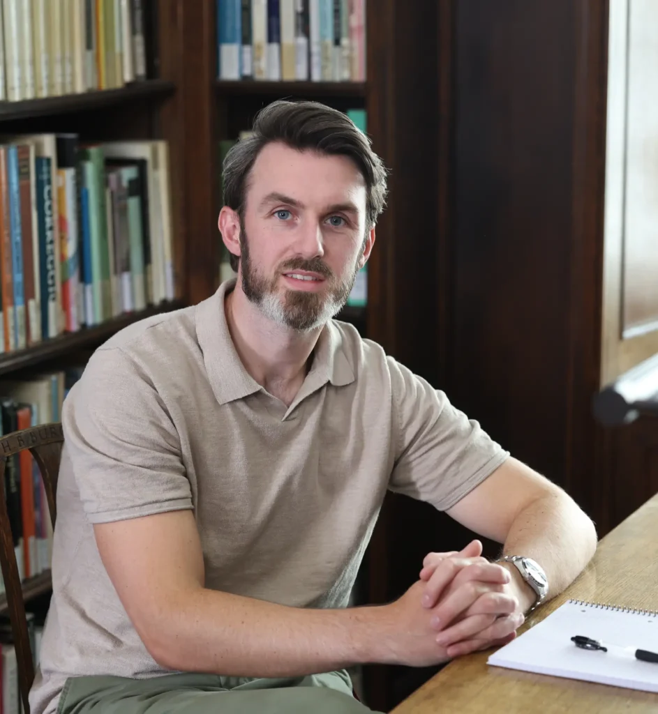 Ryan Hegarty, compassion focused therapist in Essex, seated at a table beside bookshelves during a professional portrait