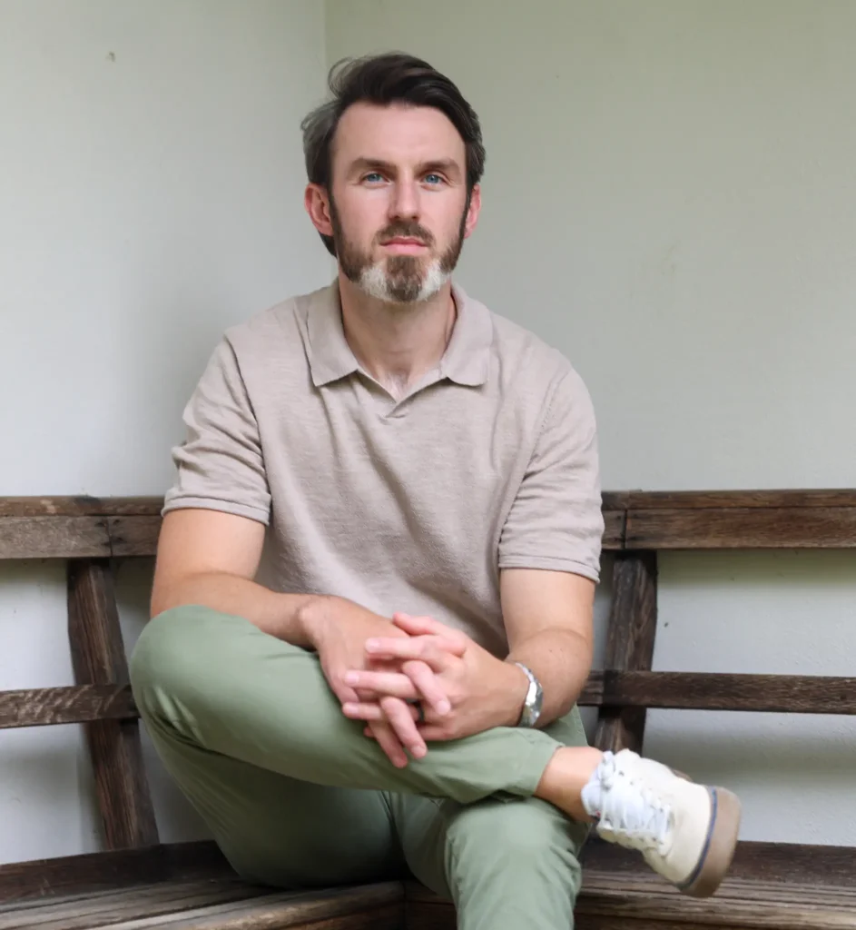 Ryan Hegarty, private CBT and EMDR therapist in Essex, seated on a wooden bench in a professional portrait