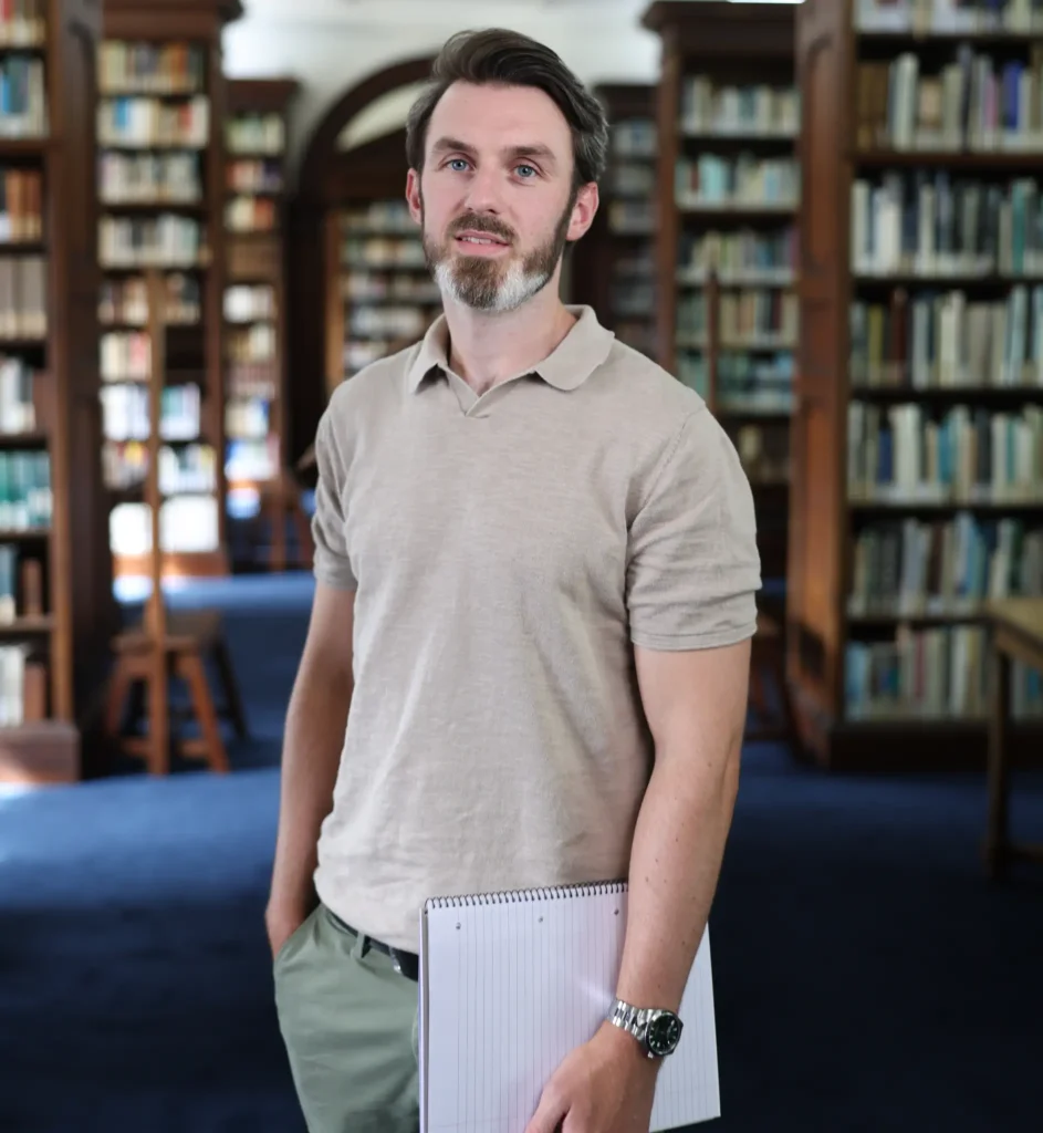 Ryan Hegarty, private therapist in Essex, standing in a library while holding a notebook